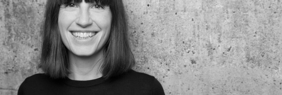 Porträtfoto von Dr. Nora Thorade die vor einer Betonmauer steht.