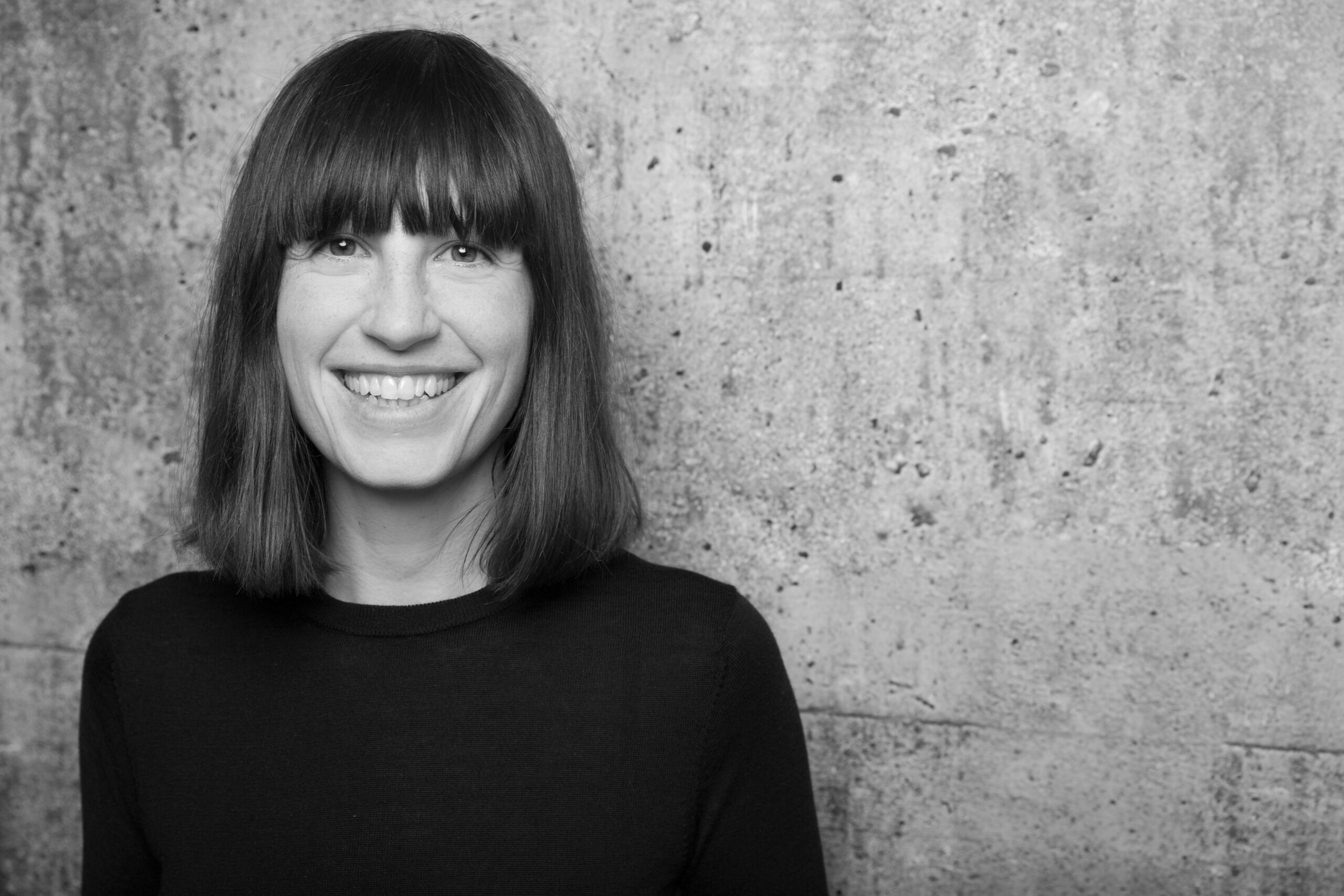 Porträtfoto von Dr. Nora Thorade die vor einer Betonmauer steht.
